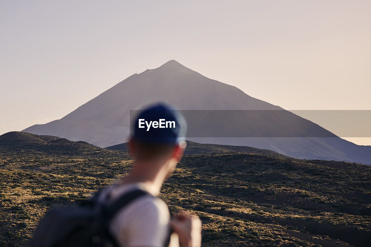 Traveler against landscape with pico de teide at dusk. young man with backpack looking on volcano.
