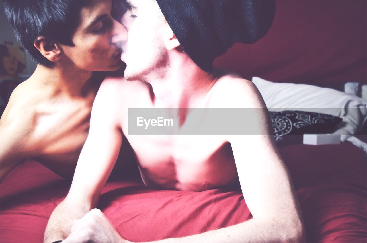 Shirtless homosexual couple kissing on bed at home