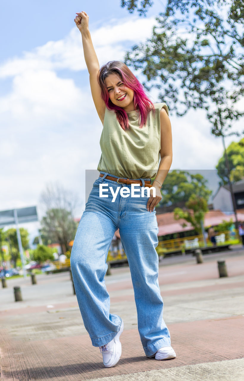 Young woman with one hand raised and smiling in park