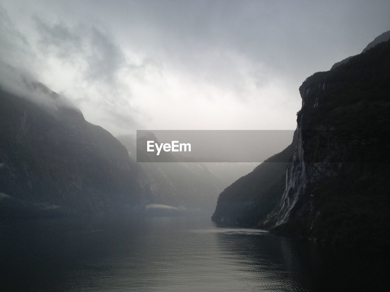 Scenic view of river amidst mountains against sky during foggy weather