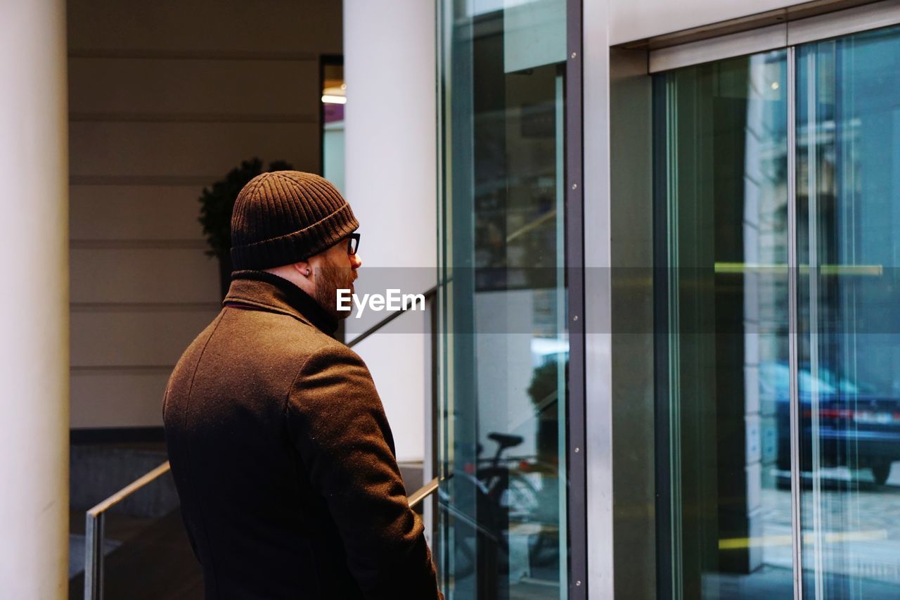 SIDE VIEW OF MAN LOOKING THROUGH GLASS WINDOW