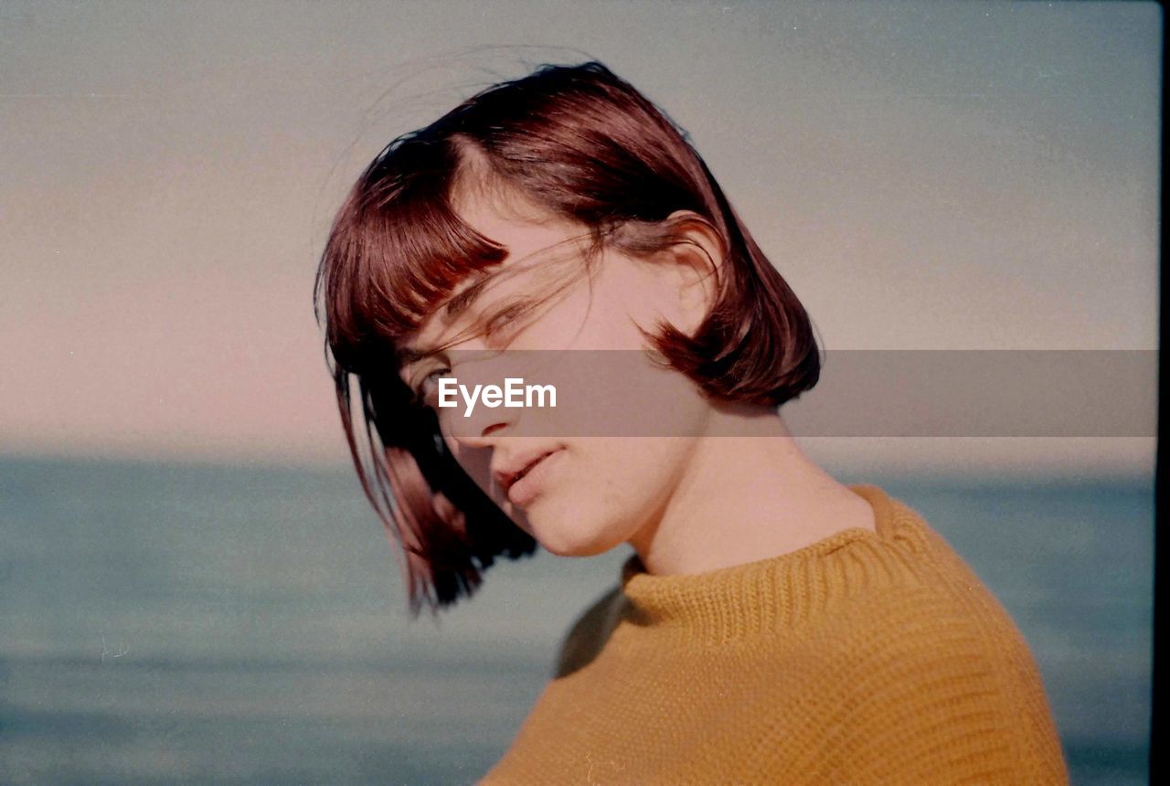 CLOSE-UP OF BEAUTIFUL YOUNG WOMAN AGAINST SEA