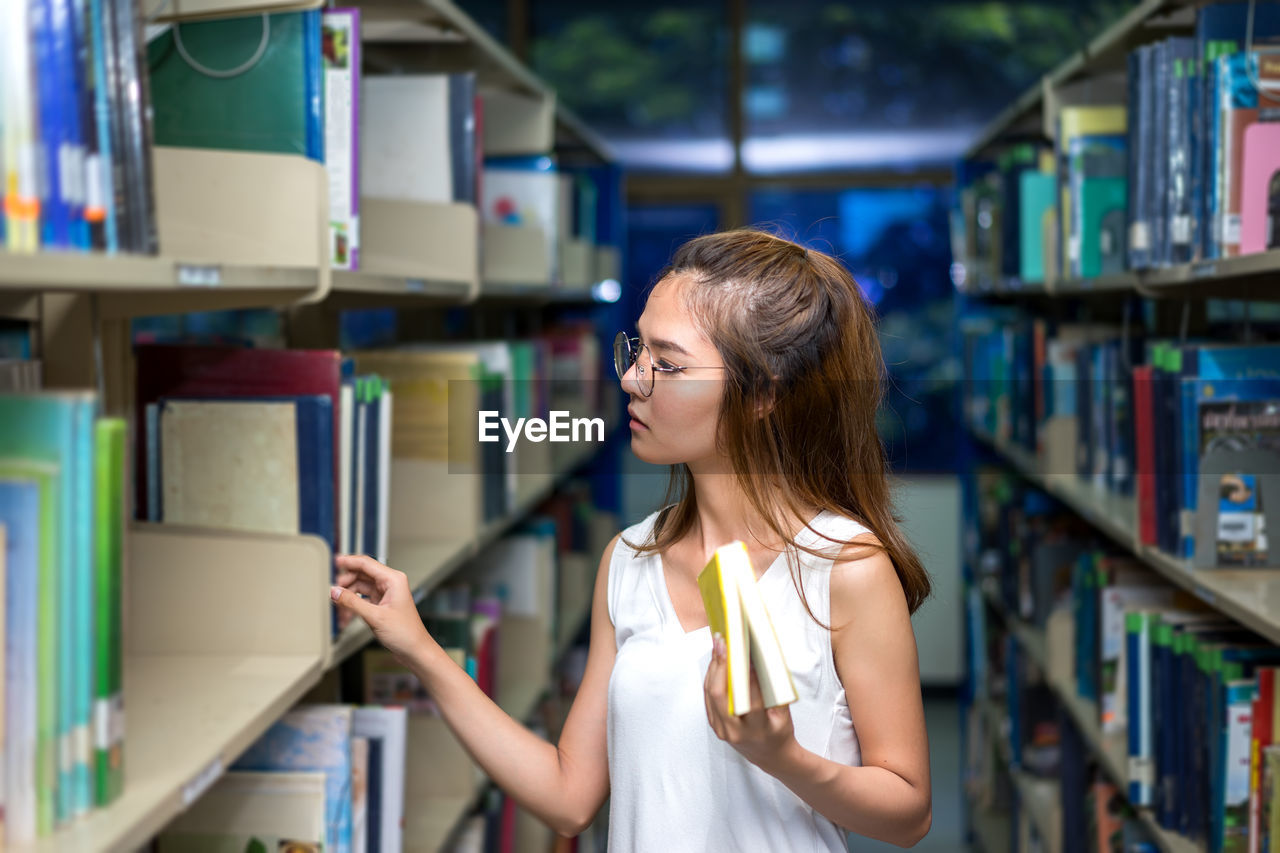 Young woman searching book on shelf in library