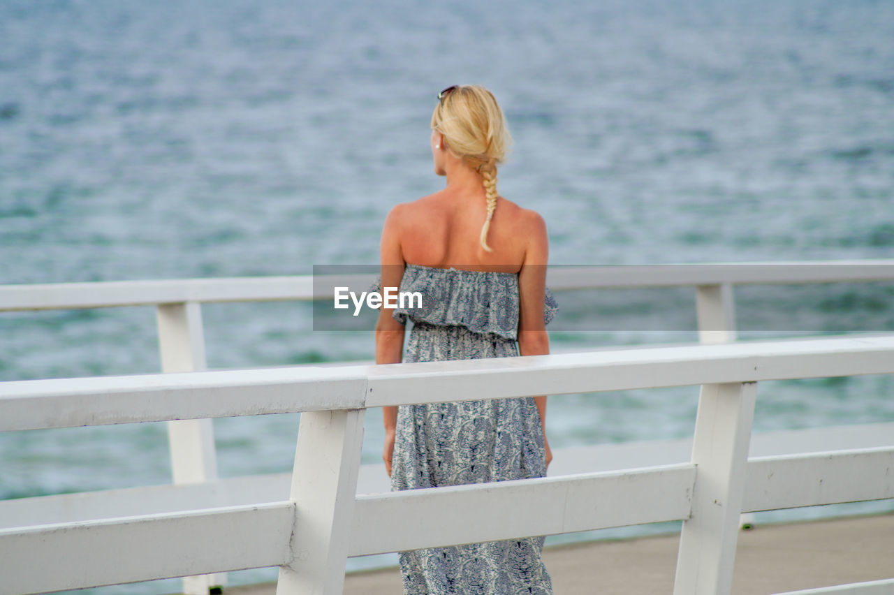 Rear view of young woman standing on pier over sea