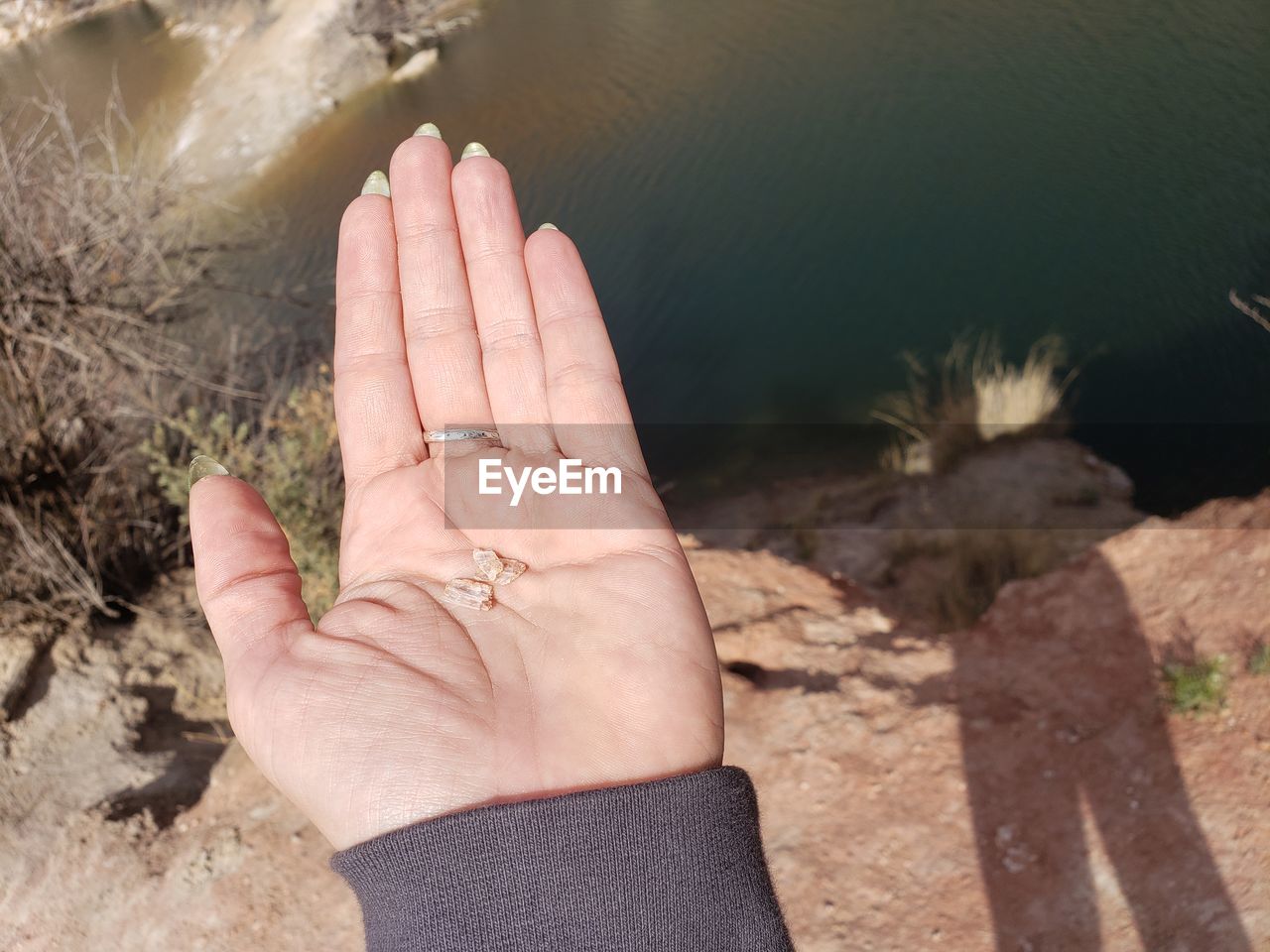 Cropped hand of person holding rock over lake