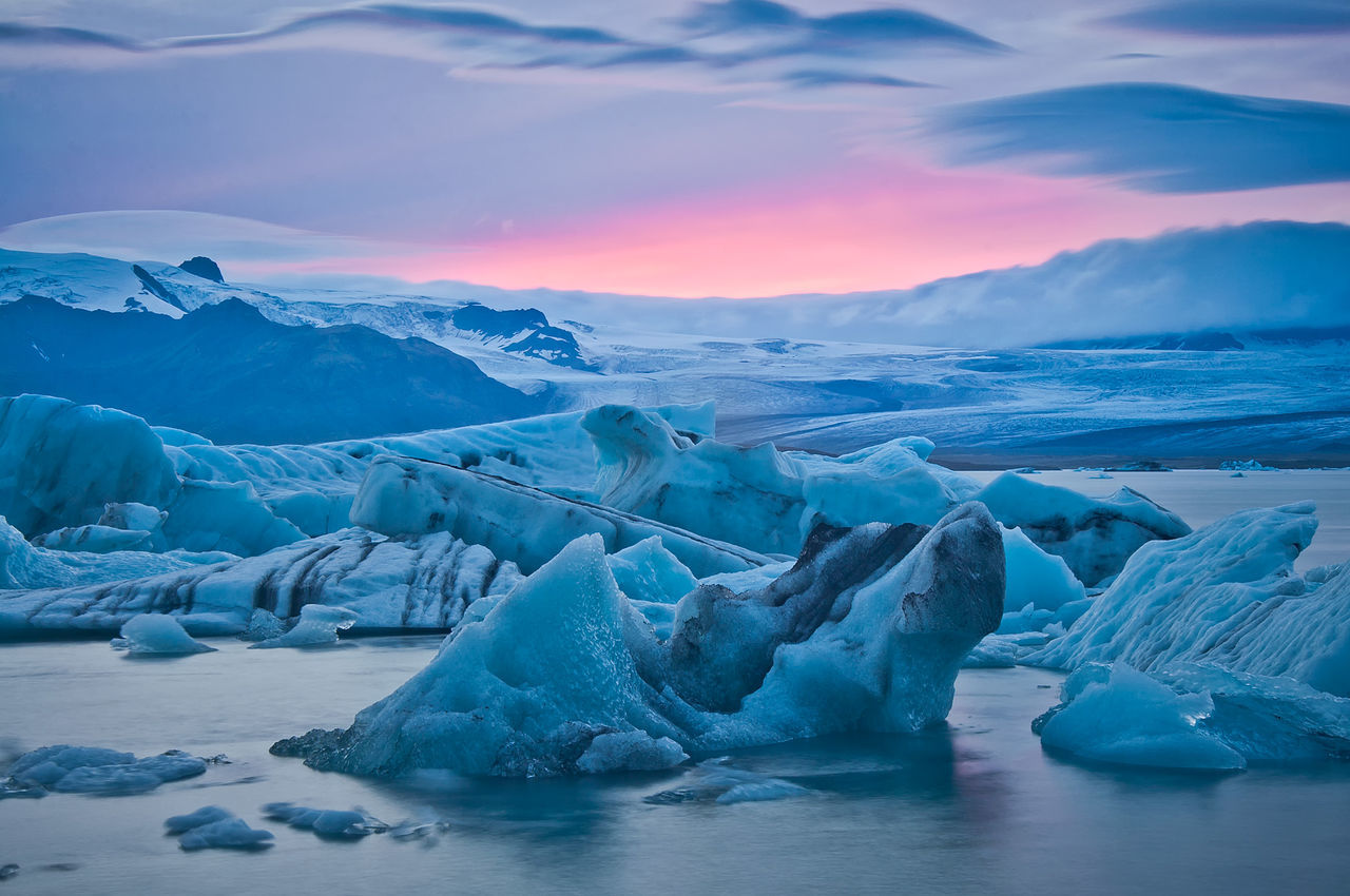 Icebergs in frozen lake against cloudy sky at sunset