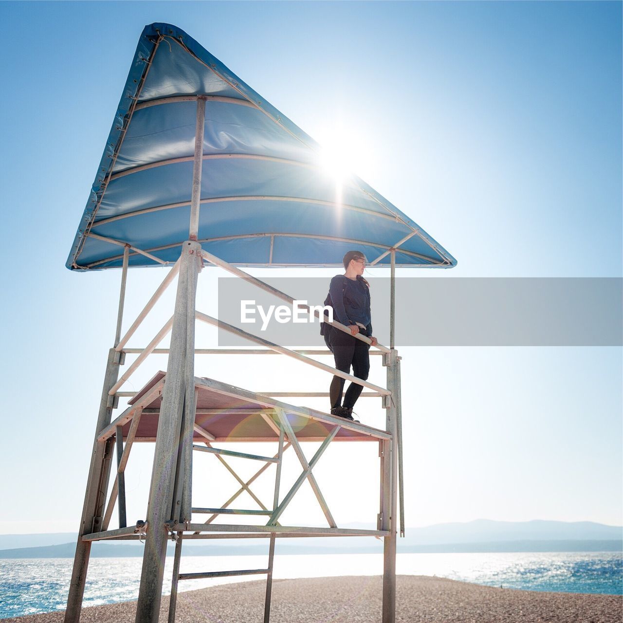 Low angle view of woman standing in lifeguard hut at beach against sky