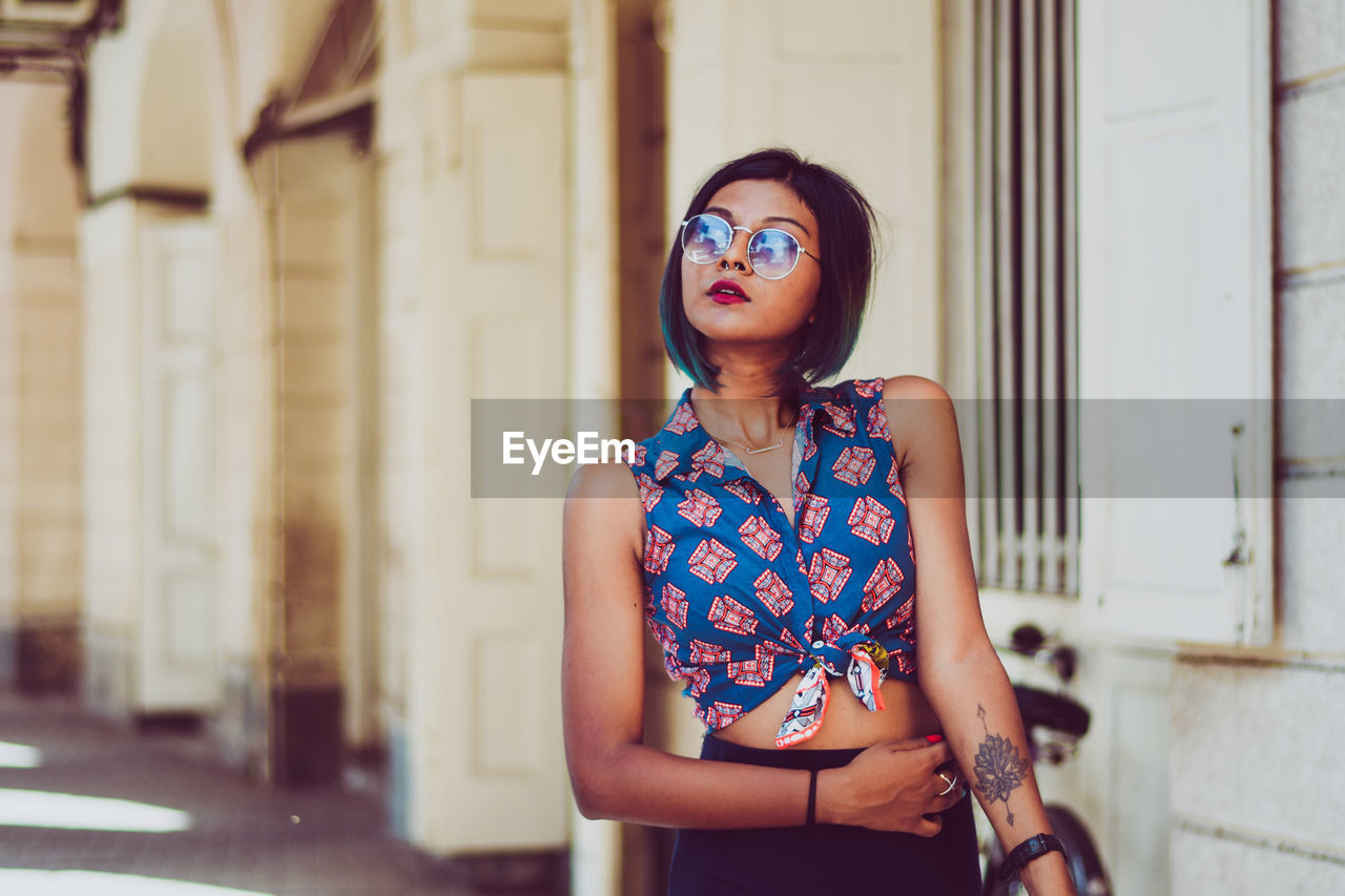 Young woman wearing sunglasses while standing by building