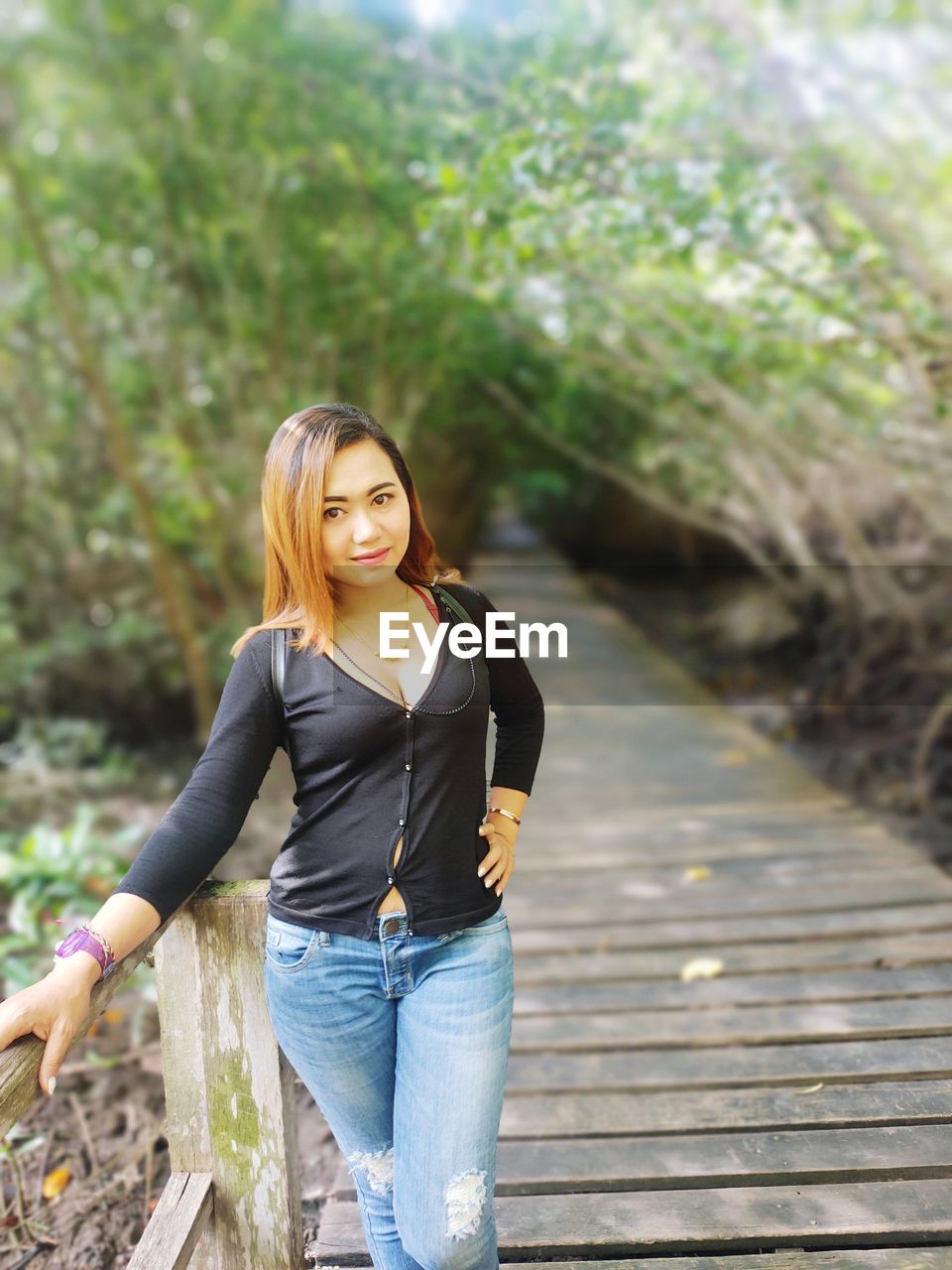 PORTRAIT OF YOUNG WOMAN STANDING AGAINST TREES