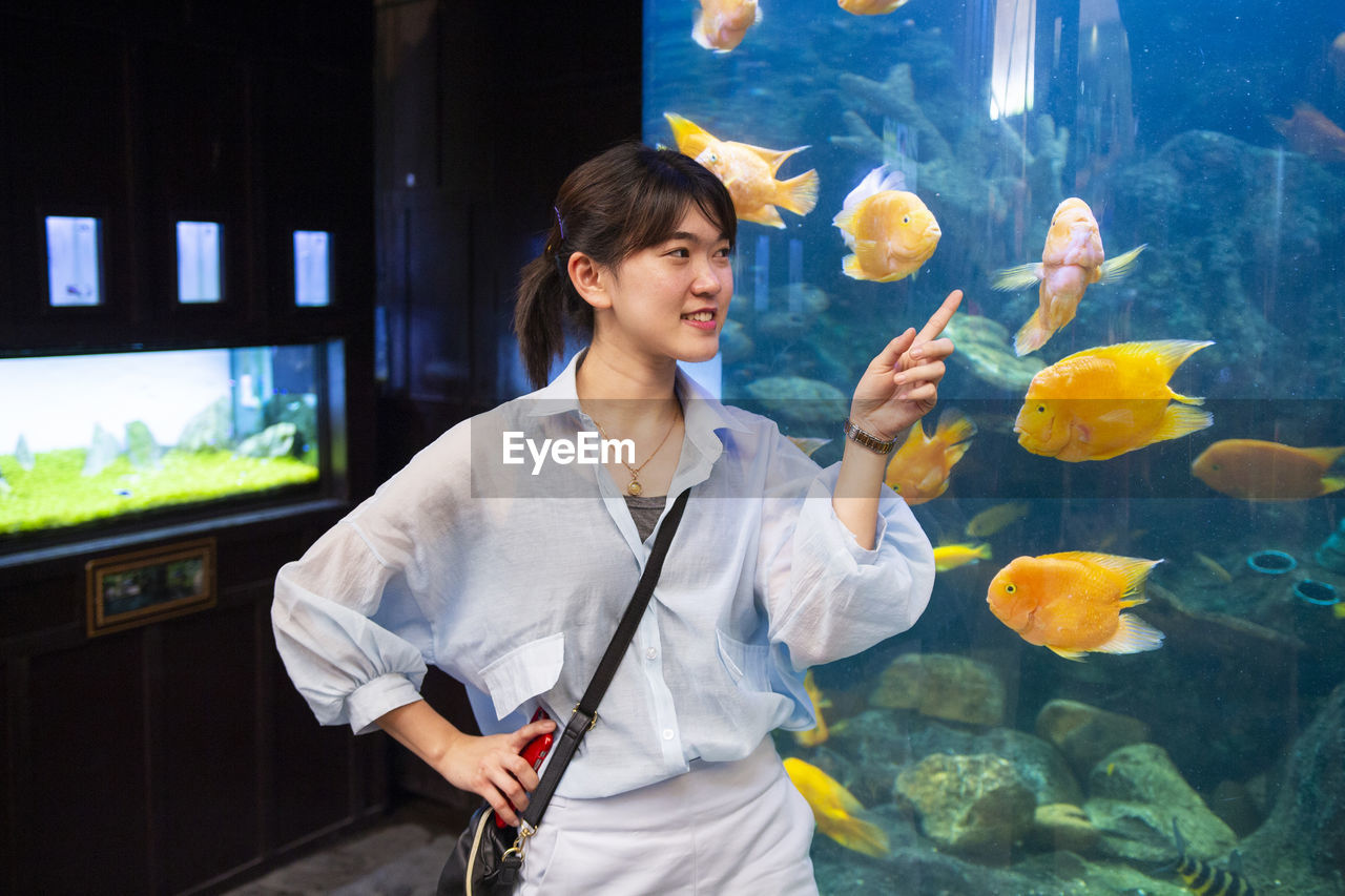 Smiling woman pointing at fish while standing in aquarium