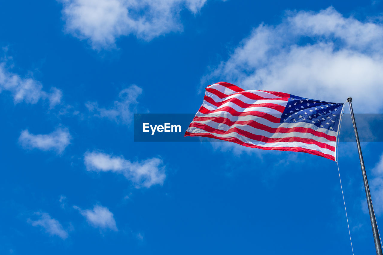 Low angle view of american flag waving against blue sky