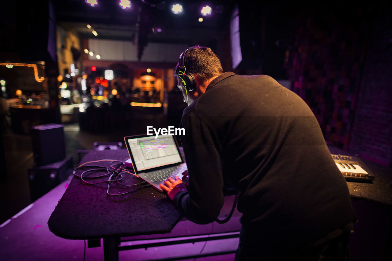 Rear view of man using laptop while standing in nightclub