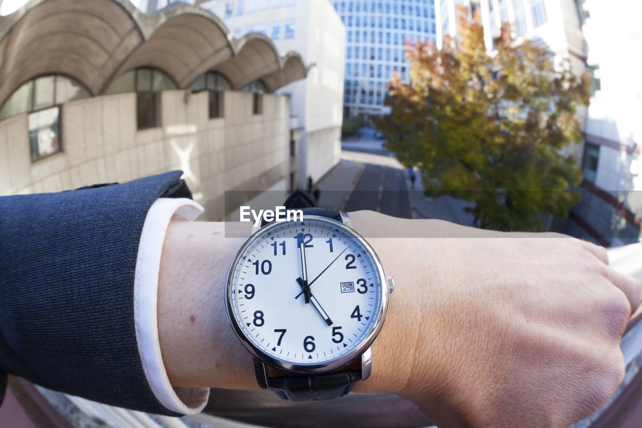 Cropped hand of businessman wearing wristwatch by railing in city