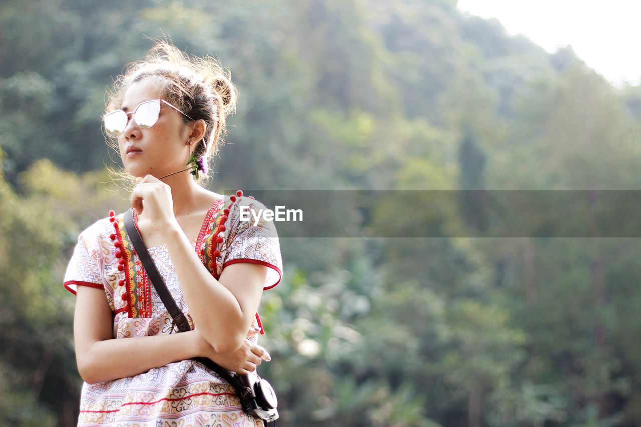 Young woman wearing sunglasses standing against mountain