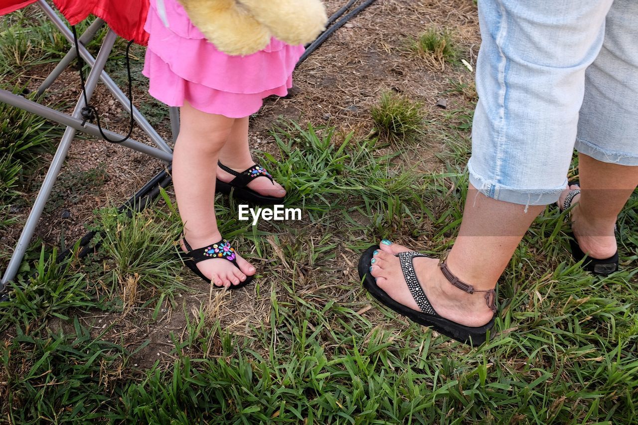 Low section of mother with daughter standing on grassy field