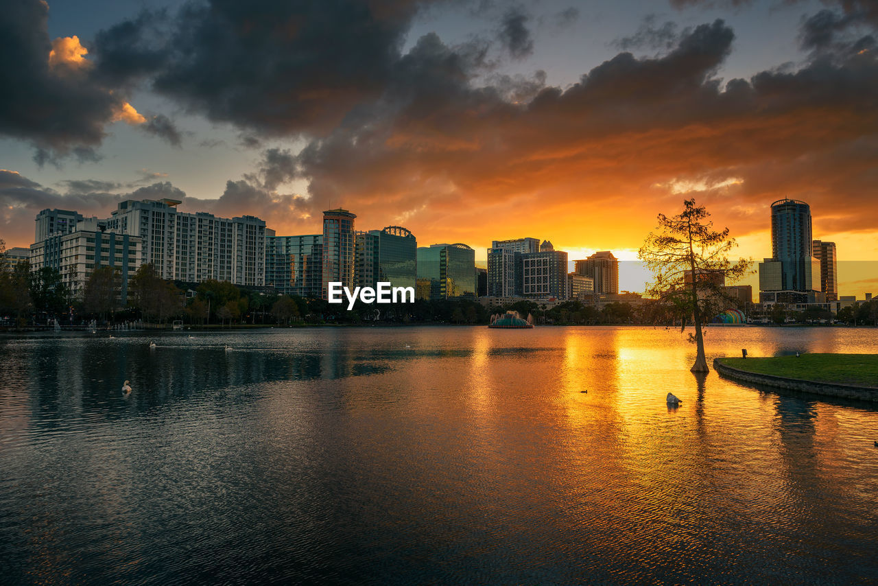 BUILDINGS BY RIVER AGAINST SKY DURING SUNSET