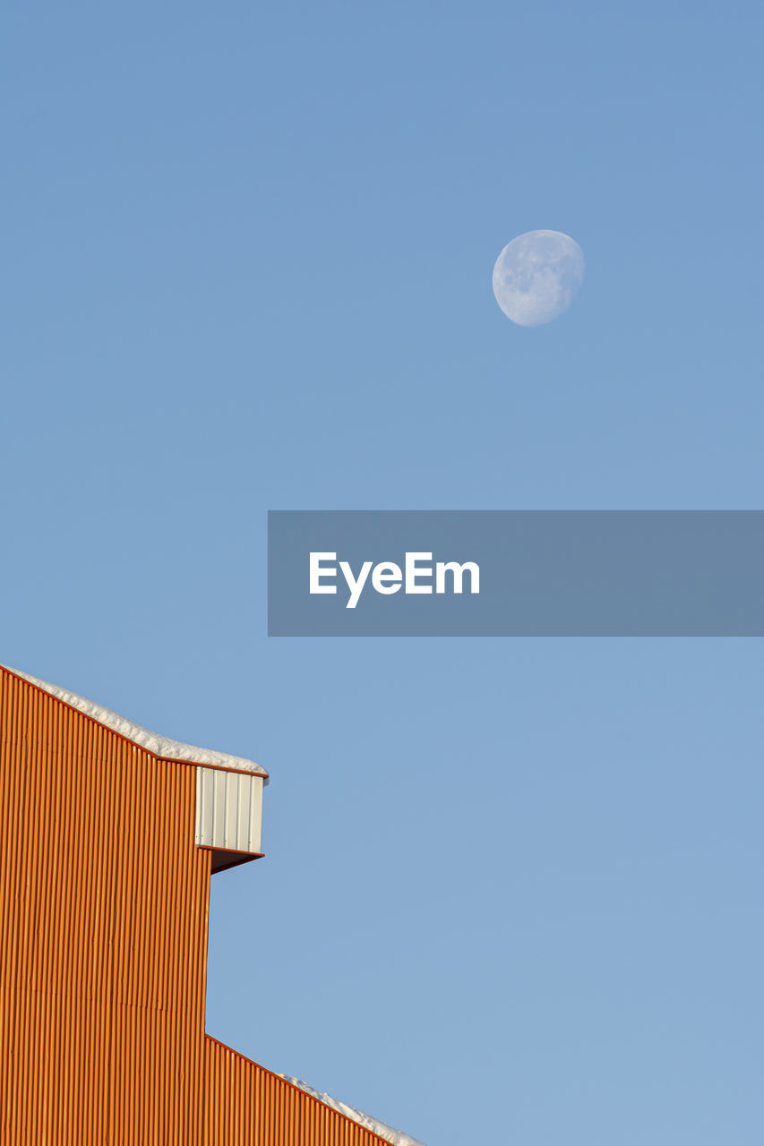 Detail shot of a house building rooftop after a snowfall in winter season, morning moon at blue sky