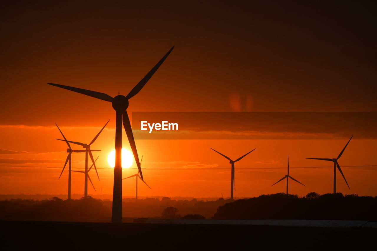 A bright red sunset through wind turbines