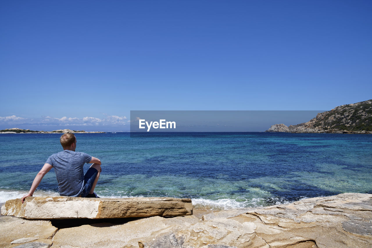 Rear view of man looking at sea against blue sky