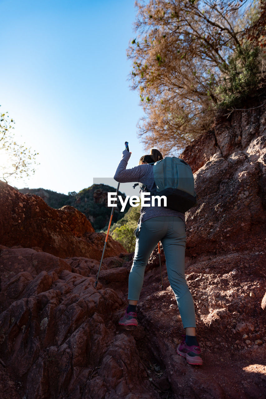 Woman climbs the mountain in the garraf natural park, supported by hiking sticks.