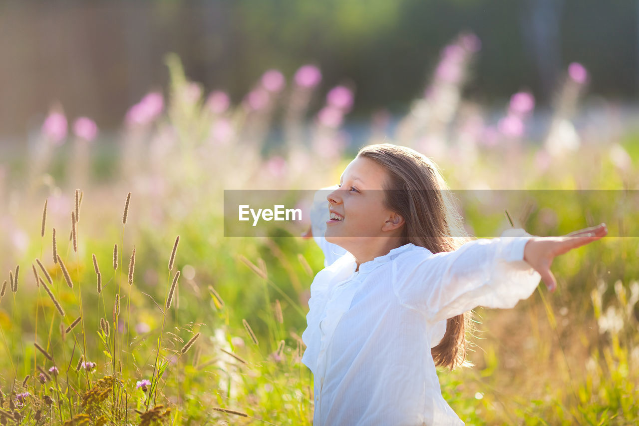 13 year old girl stands on blooming field in summer time and enjoys clean air and freedom