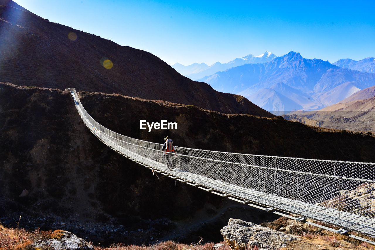 Man walking on footbridge against mountain