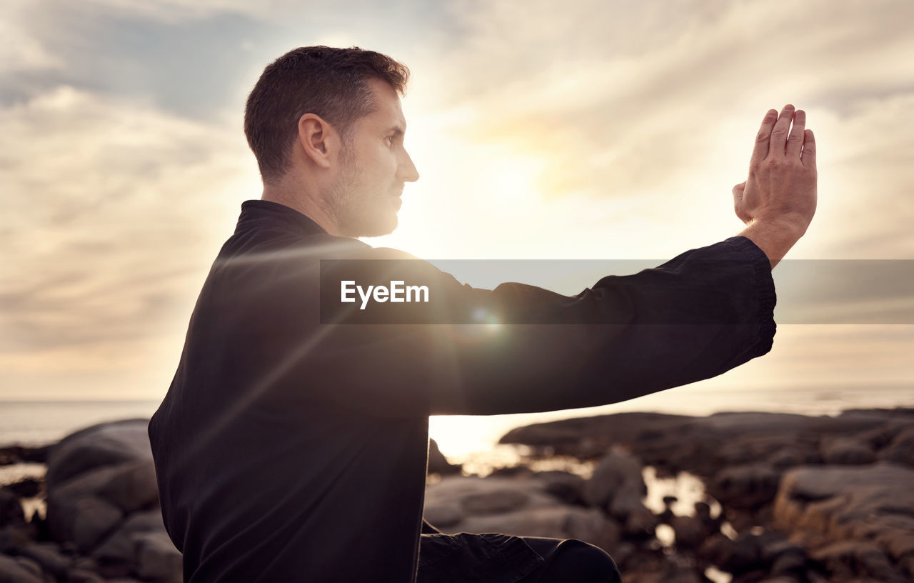 sky, one person, adult, men, sunset, nature, cloud, sunlight, back lit, sun, limb, person, land, romance, lens flare, outdoors, relaxation, success, rock, young adult, arm, beach, human limb, copy space, emotion, business, lifestyles, standing, dusk, beauty in nature, side view, waist up, hand