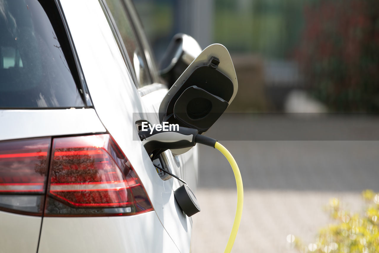 Plug in adapter in car charge battery of electric car next to a charging station with yellow cable