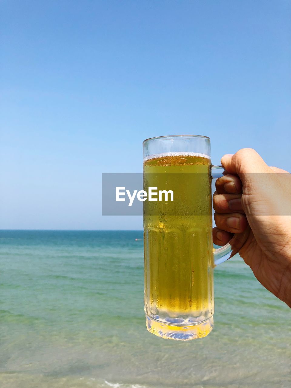 Close-up of hand holding beer glass against clear sky