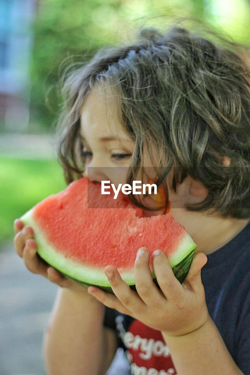 Boy eating watermelon while sitting at yard