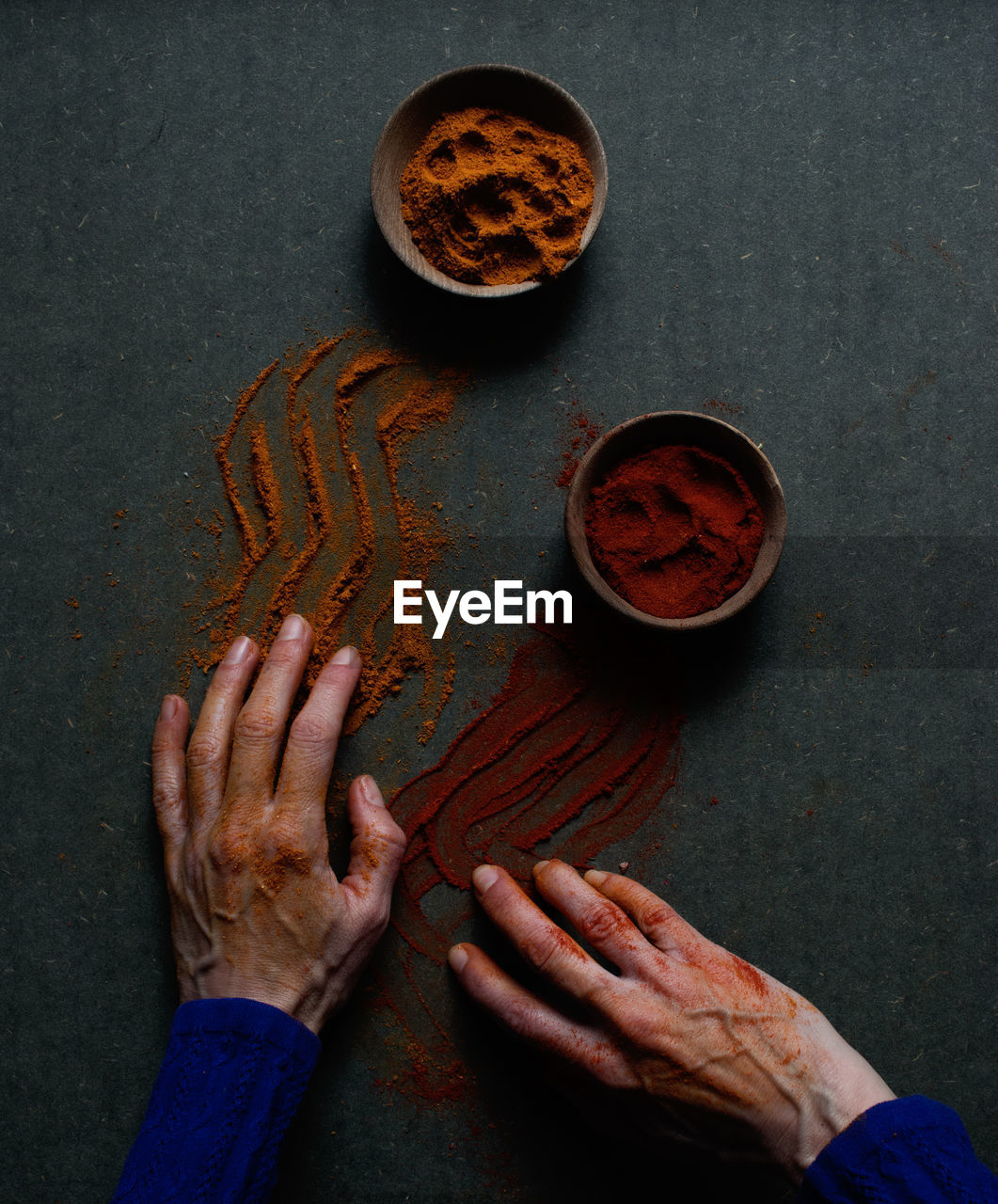 Top view of crop unrecognizable person touching table with spilled paprika and cinnamon powders