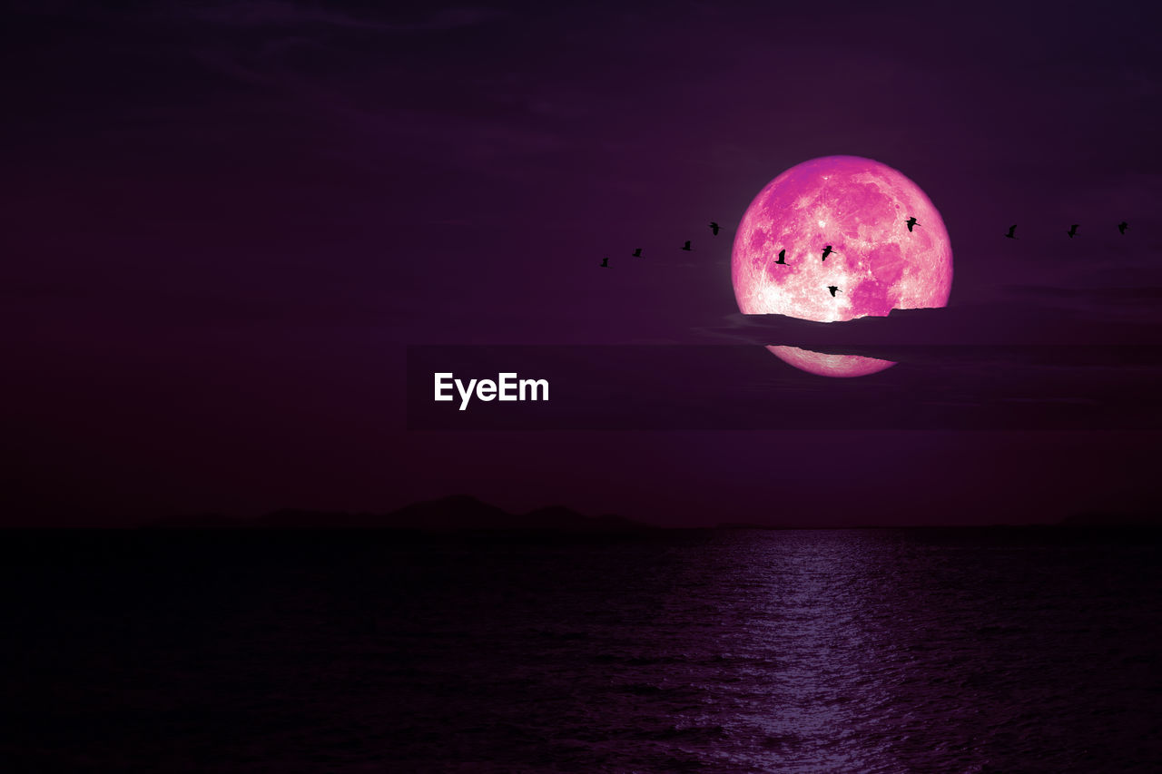Full snow pink moon on night sky back cloud over dark sea, elements of this image furnished by nasa