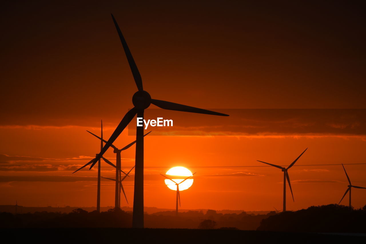 A bright red sunset through wind turbines