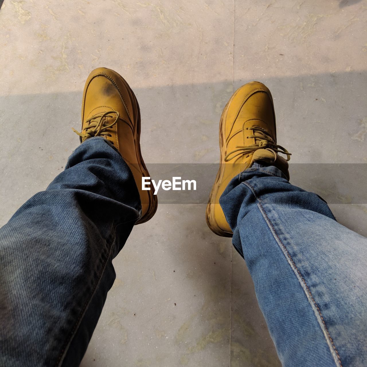 LOW SECTION OF MAN WEARING SHOES STANDING AGAINST YELLOW