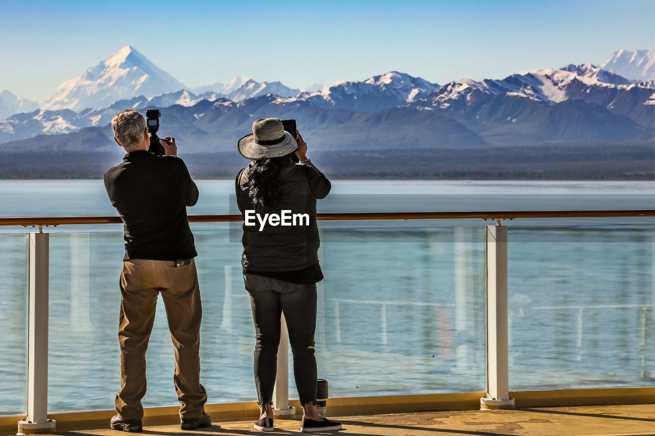 Rear view of man and woman photographing snowcapped mountain
