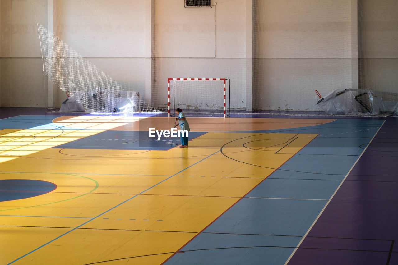 Side view of woman cleaning basketball court