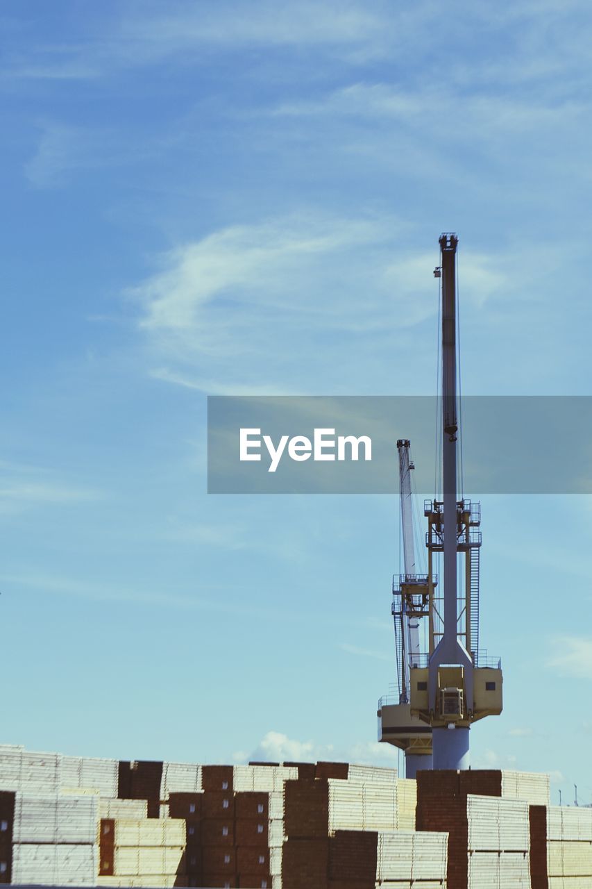 Low angle view of containers and crane at commercial dock against sky