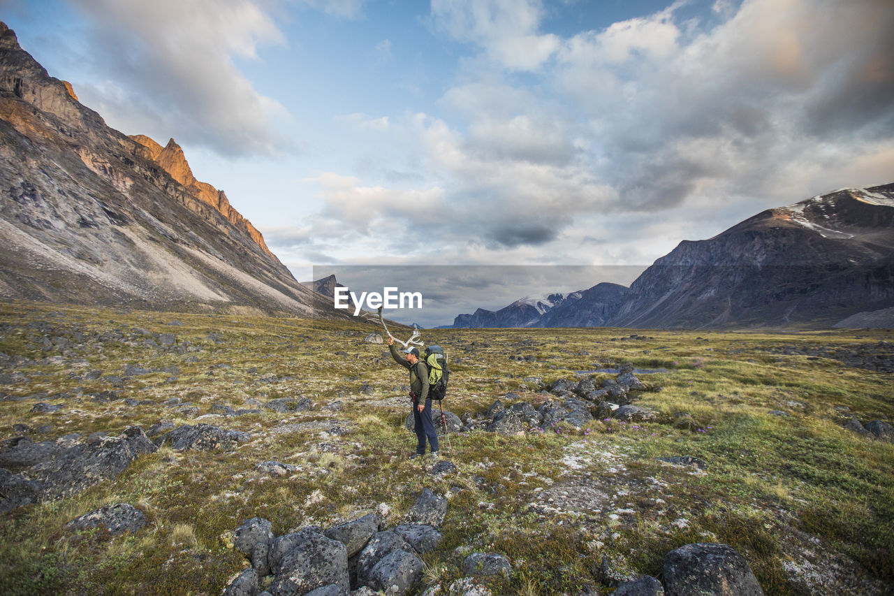 Backpacker standing in mountain pass holding caribou antler on head.