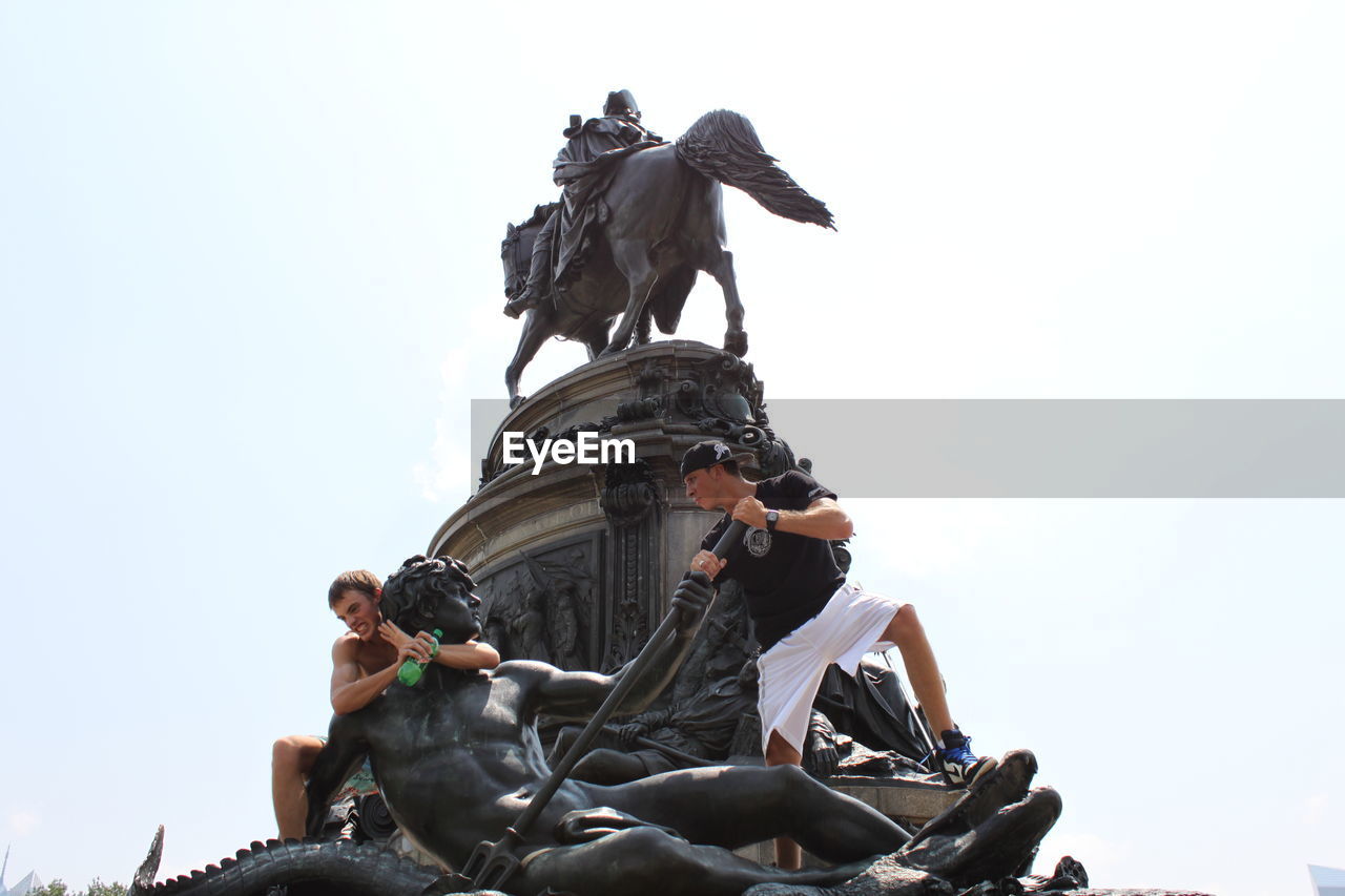 Low angle view of men climbing on statues against clear sky