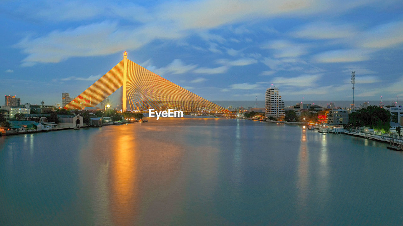 illuminated bridge over river in city against sky