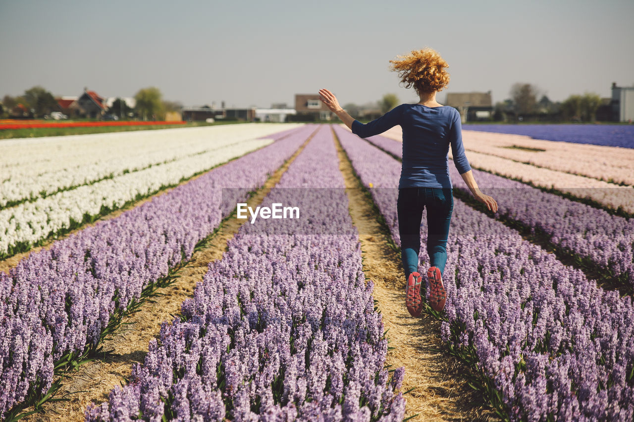 Rear view of woman jumping in flower field