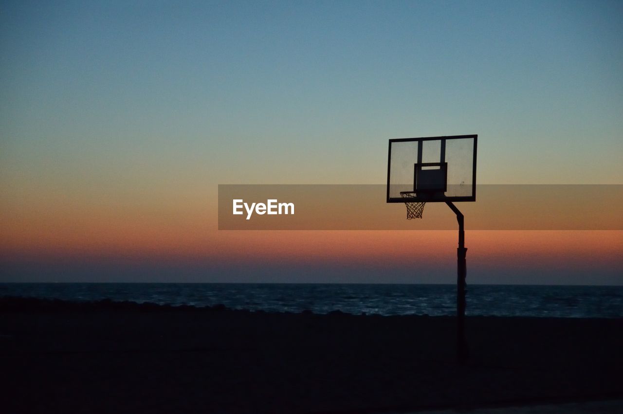 Silhouette basketball hoop at beach against sky during sunset