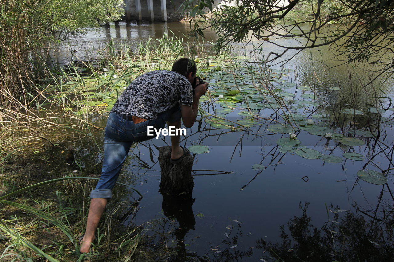 Rear view of man photographing over lake