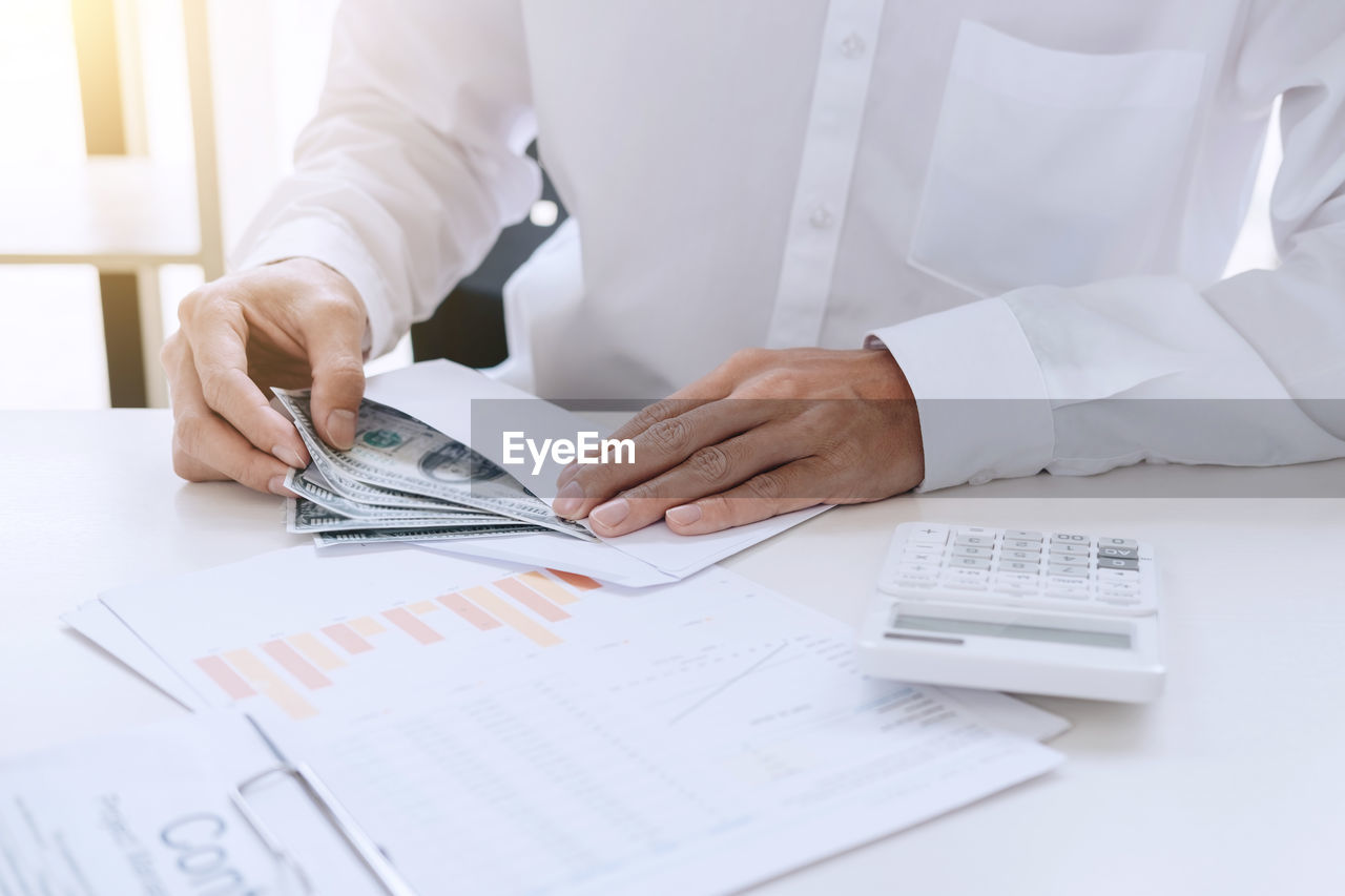 Midsection of businessman counting paper currency at desk in office