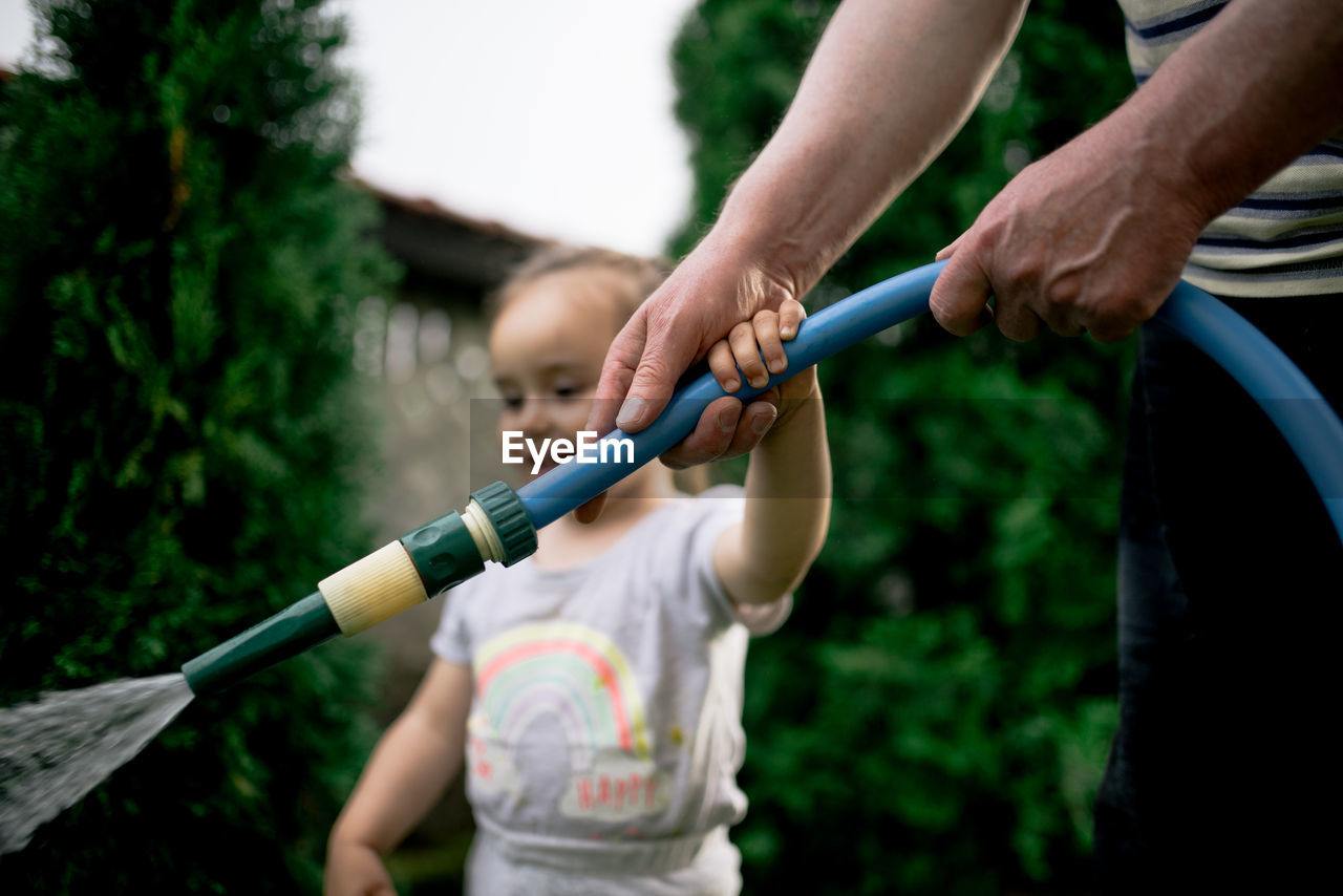 Little girl watering garden with her grandfather.