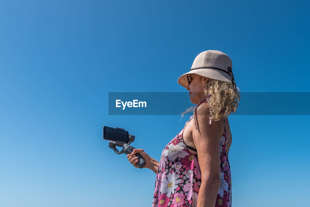 Back view of a woman using a mobile attached with a gimbal outdoors with the blue sky