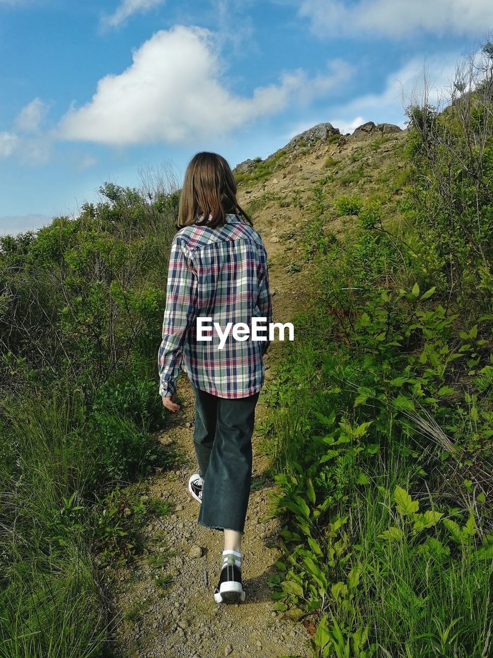 Girl in checkered shirt going forward on the mountain path against the sky