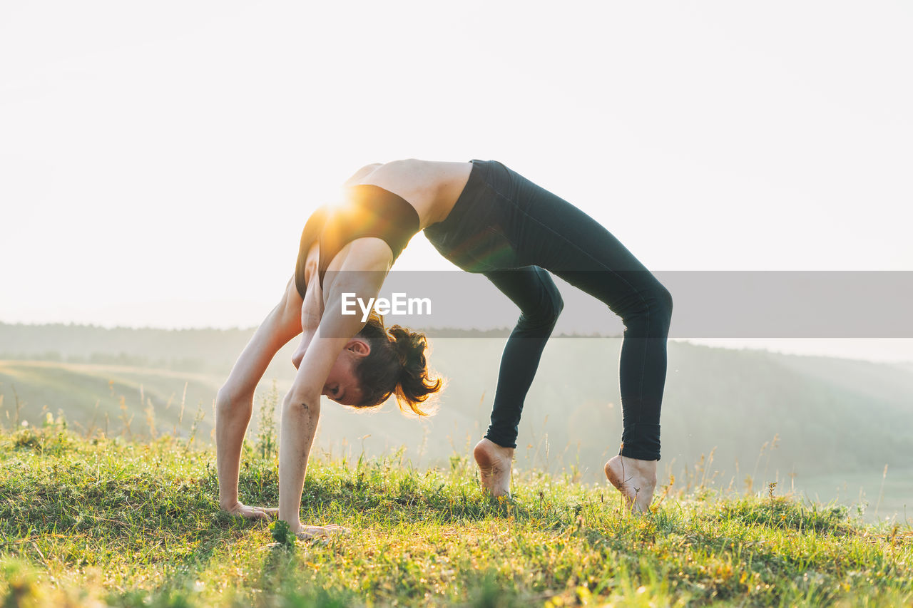 Rear view of woman with arms outstretched on field against sky