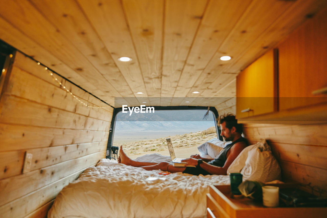 Young man on bed with laptop in camper van in northern california.