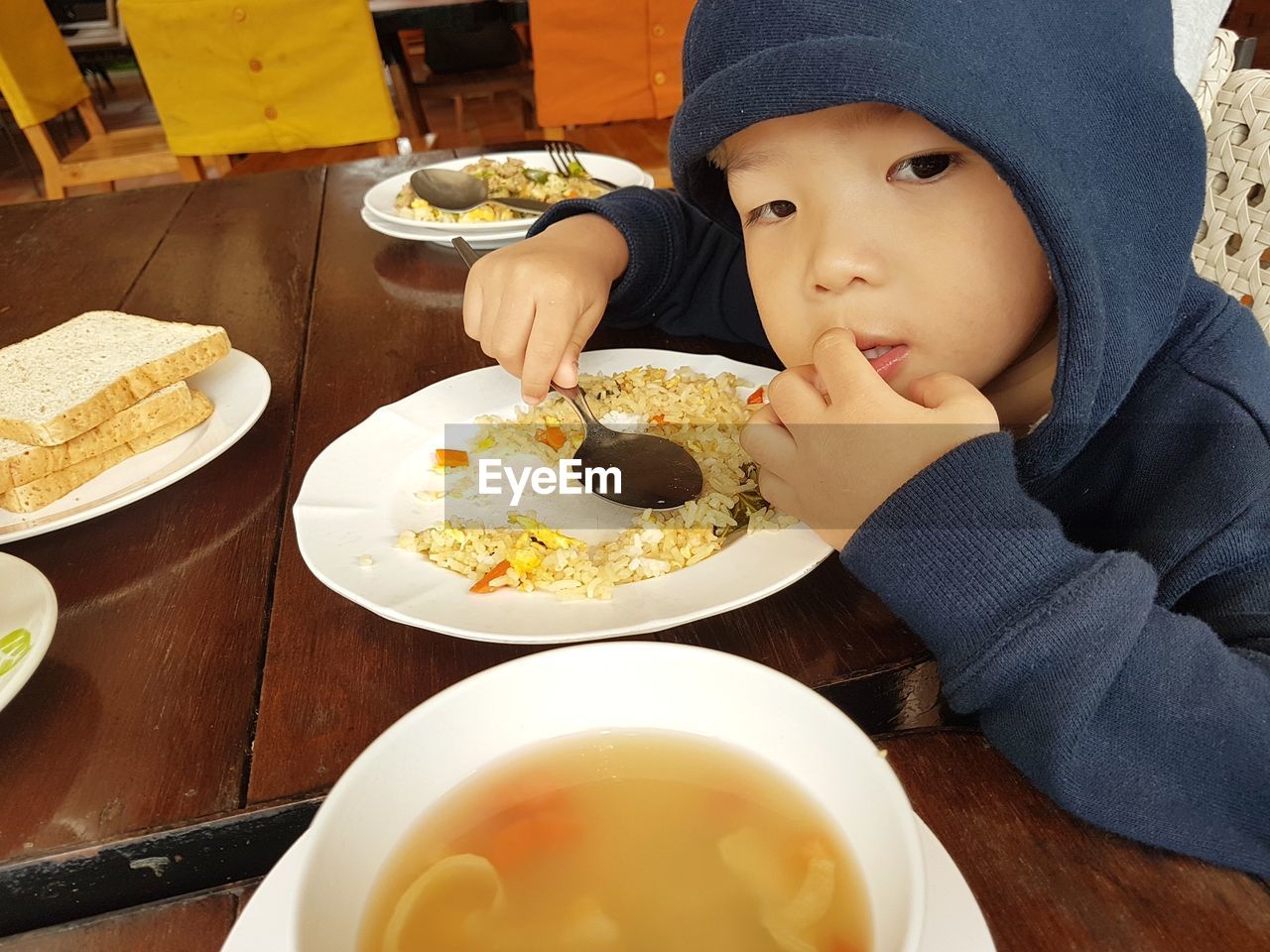 Close-up of cute boy wearing hooded shirt having meal at home